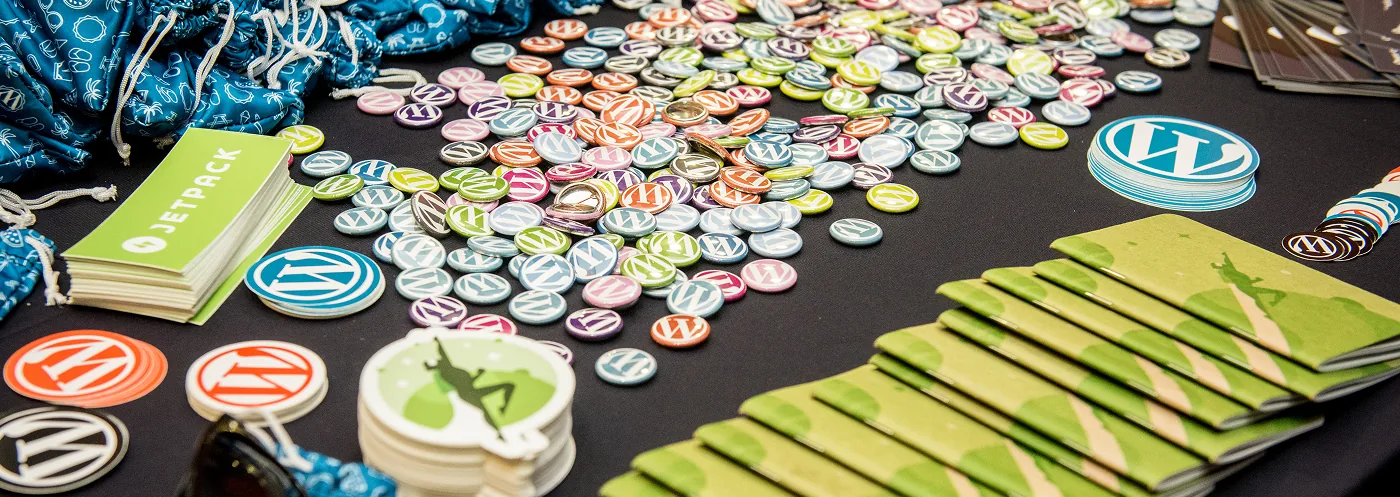 Mesa com vários bottons, adesivos e brindes do WordCamp